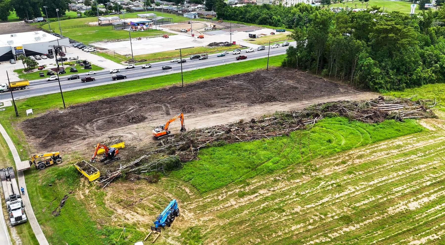 Aerial view of a large commercial land clearing and site work project along a highway corridor, with multiple pieces of heavy equipment