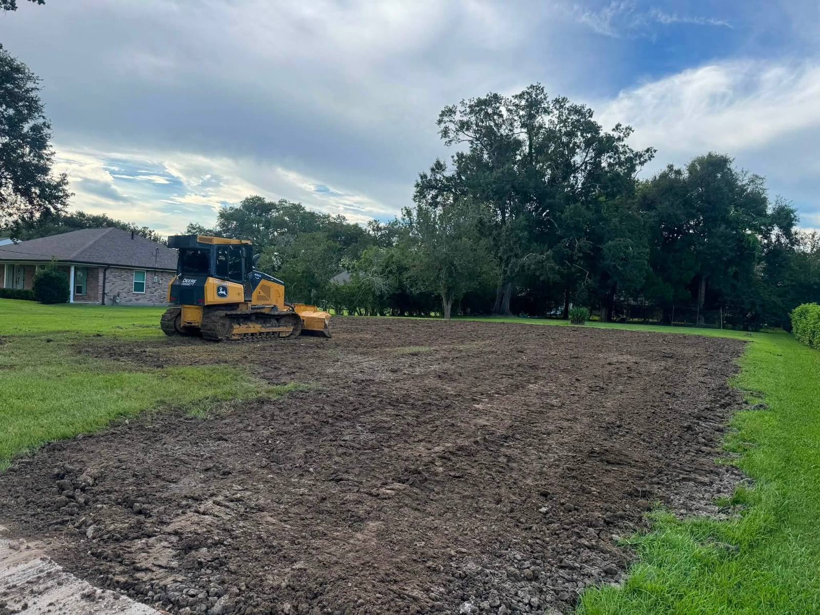 John Deere dozer grading a cleared residential lot next to a home