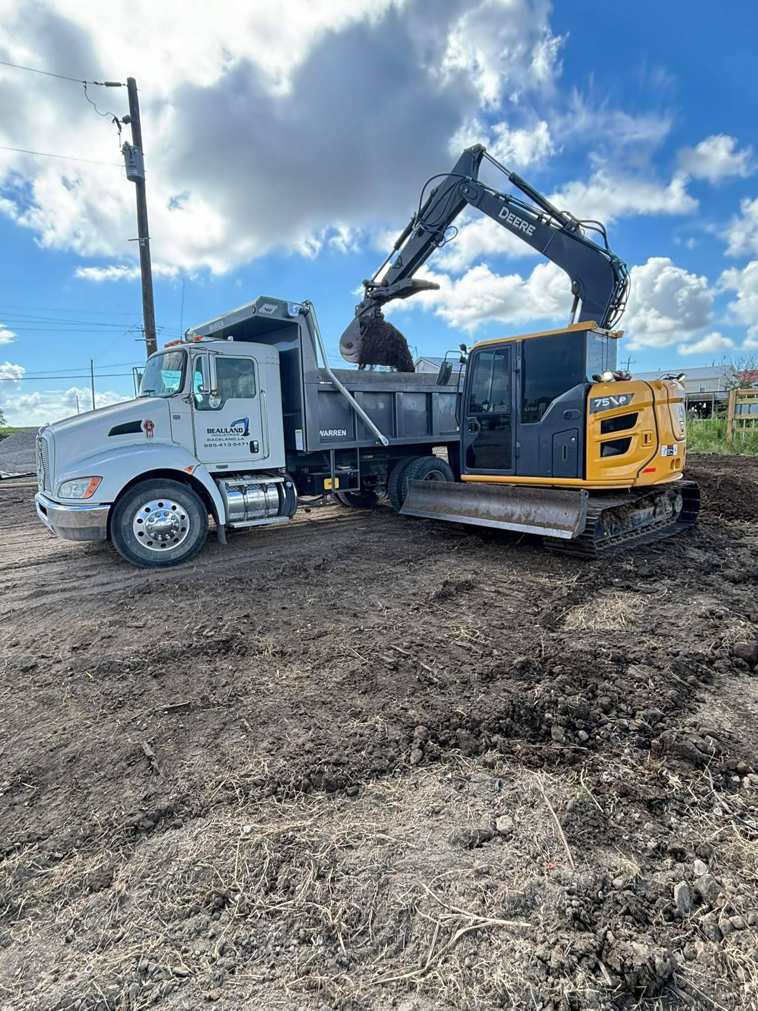 Beauland Industries dump truck being loaded by a John Deere excavator on a South Louisiana job site