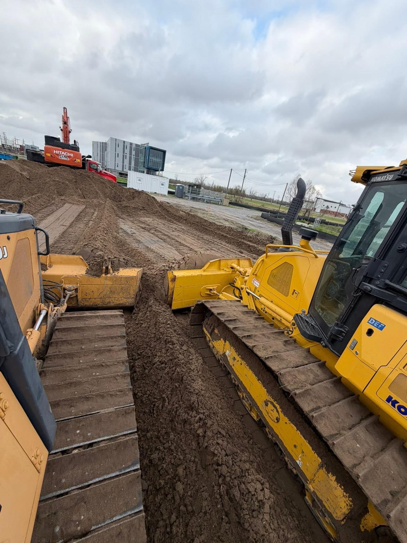 Two bulldozers and an excavator working together at a large commercial site